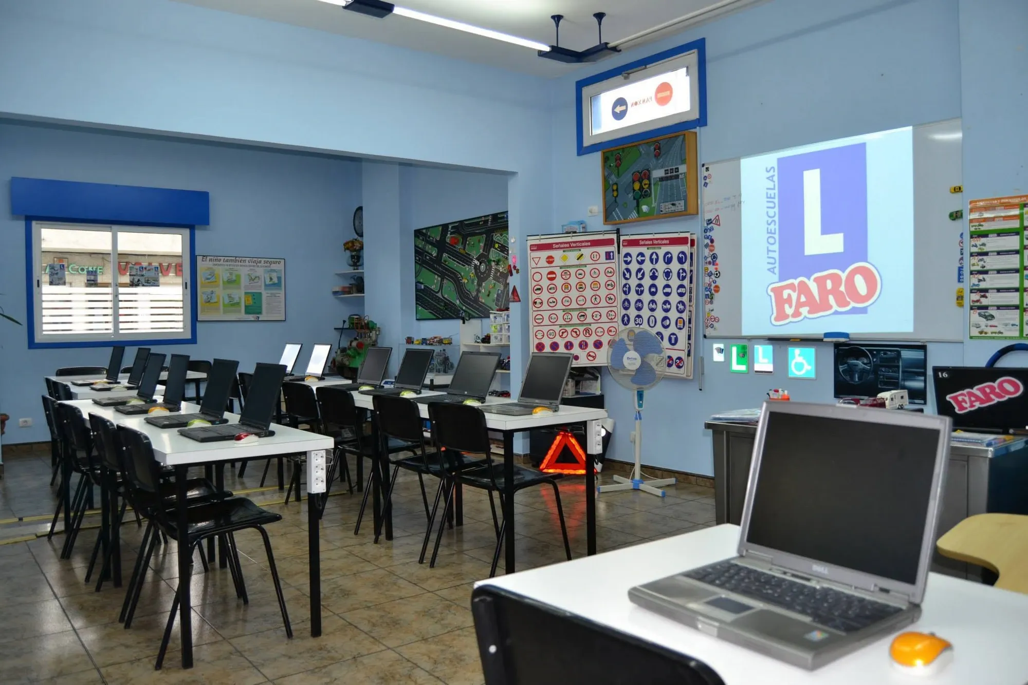 Aula de teórica en Panxón con ordenadores portátiles, láminas de señales y proyector con el logo de Autoescuelas Faro